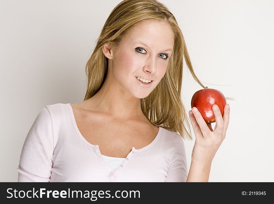 A blond girl is smiling and holding a red apple. A blond girl is smiling and holding a red apple