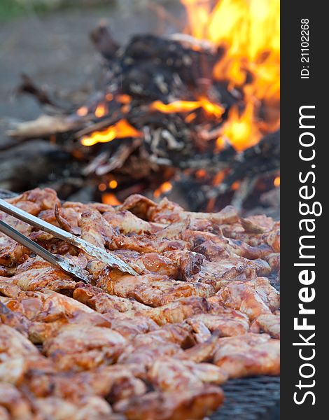 A vertical close up of chicken pieces being grilled on an open fire outdoors. A vertical close up of chicken pieces being grilled on an open fire outdoors