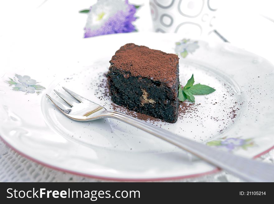 A piece of chocolate cake dusted with cocoa in a white plate and fork - spot metering. A piece of chocolate cake dusted with cocoa in a white plate and fork - spot metering