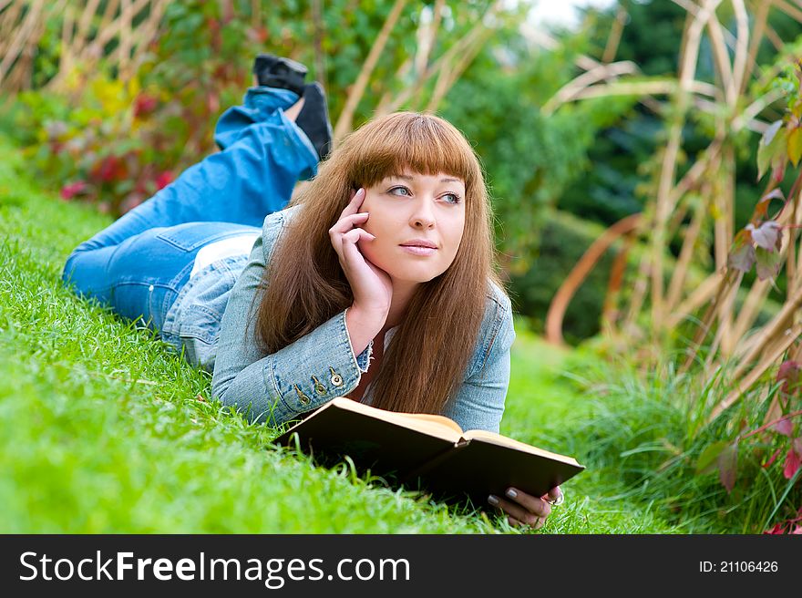 Young woman reading a book lying on the grass in the park