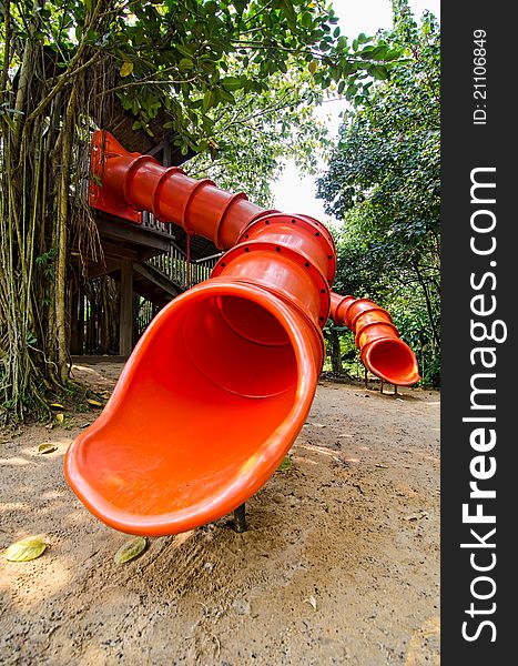 Photo of red colorful slide and a treehouse in garden or backyard of nursery school play area. Photo of red colorful slide and a treehouse in garden or backyard of nursery school play area