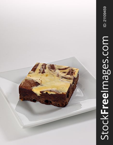 A single cream cheese brownie square shot in the studio on a white plate.