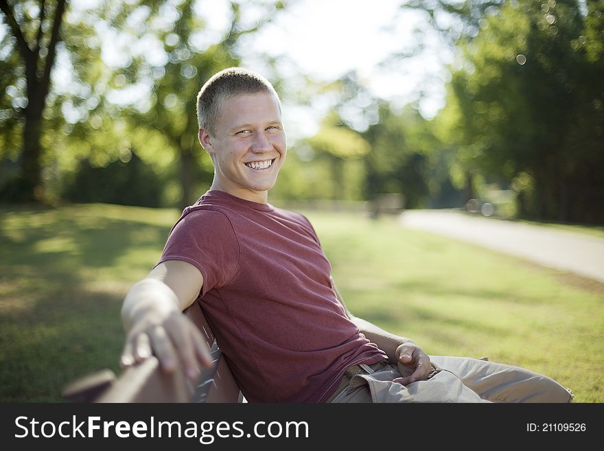 Handsome young man sitting on a bench smiling. Candid. Handsome young man sitting on a bench smiling. Candid.