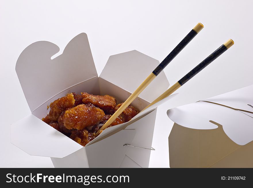 Orange chicken in a white takeout container and chopsticks, isolated on white. There is also an empty take out container to the side. Orange chicken in a white takeout container and chopsticks, isolated on white. There is also an empty take out container to the side.