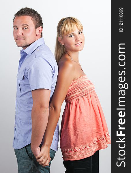 Portrait of a happy young couple standing back to back over a white background