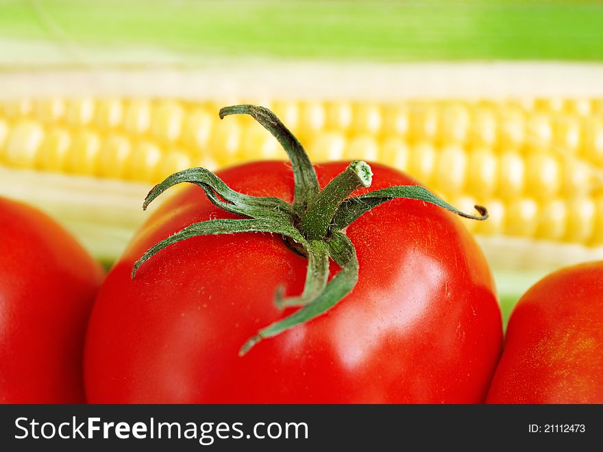 Macro of red tomato with green leaves and corn on blurred background. Macro of red tomato with green leaves and corn on blurred background
