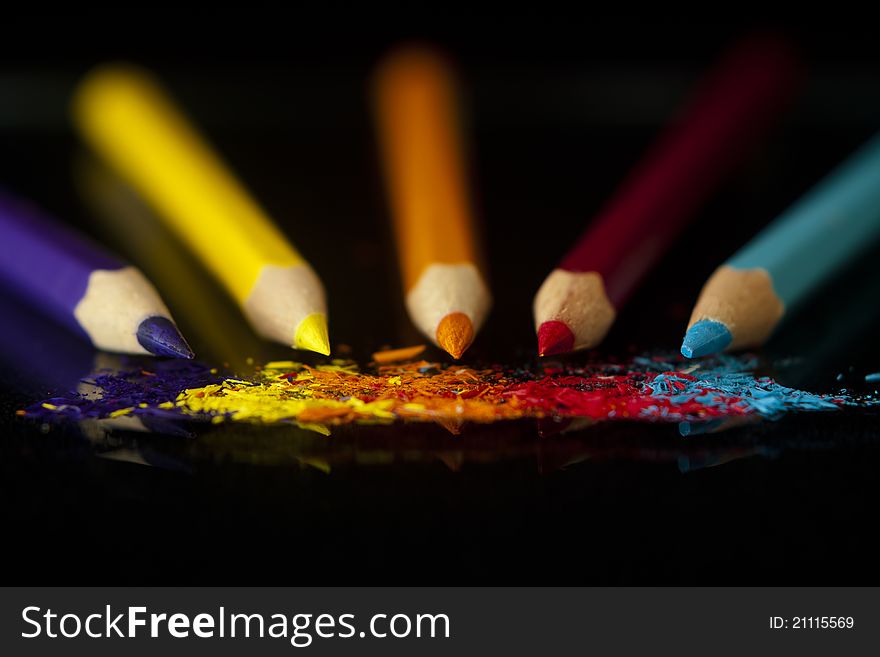 A set of colouring pencils lying behind their respective shavings.