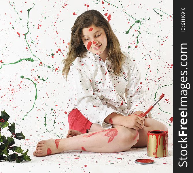 An attractive preteen surrounded by splattered red and green paint looking at that which is on herself. An attractive preteen surrounded by splattered red and green paint looking at that which is on herself.