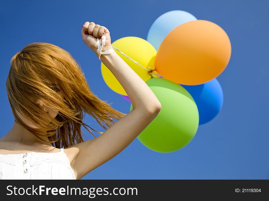 Redhead girl with colour balloons at blue sky background.