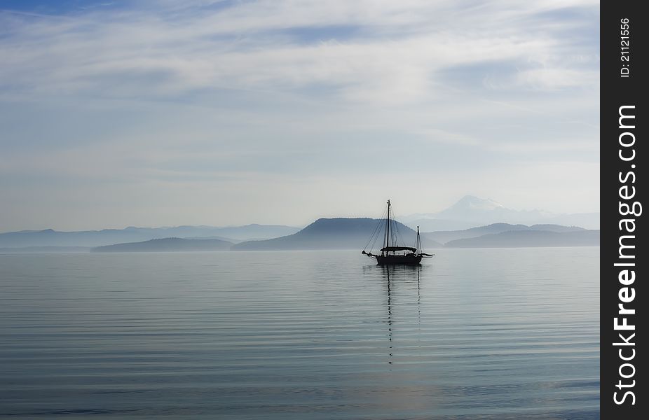 Ship in morning fog, an island and mountains ar in the background, reflection of mast in the water. Lopez Island Washington state. Ship in morning fog, an island and mountains ar in the background, reflection of mast in the water. Lopez Island Washington state