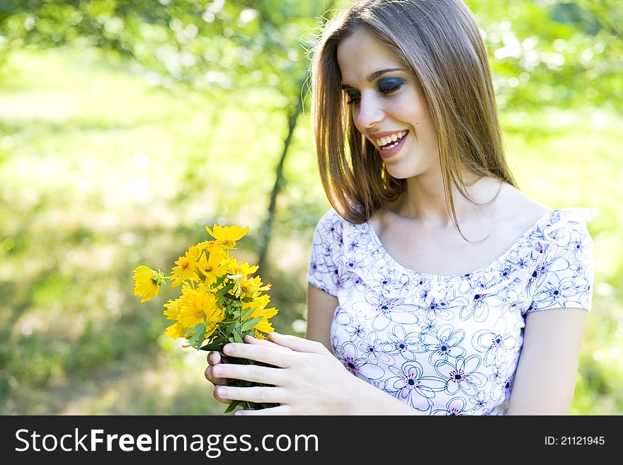 Portrait of a happy young girl smiling and holding orange flowers in her hands outdoor in summertime