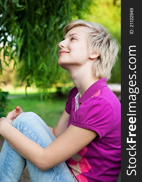 Pretty smiling girl alone sitting on the bench in the park. Pretty smiling girl alone sitting on the bench in the park