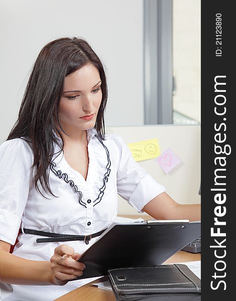 Businesswoman sitting at her desk with a clipboard and pen in the office. Businesswoman sitting at her desk with a clipboard and pen in the office