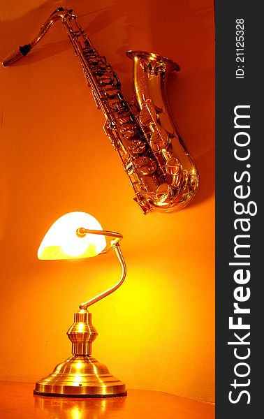 Saxophone on the orange wall next to lamp. Cafe decoration - indoor. Saxophone on the orange wall next to lamp. Cafe decoration - indoor