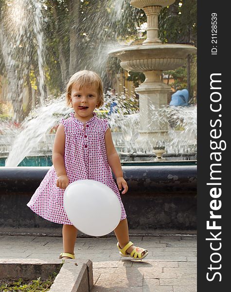 The little girl with a ball plays near a fountain. The little girl with a ball plays near a fountain