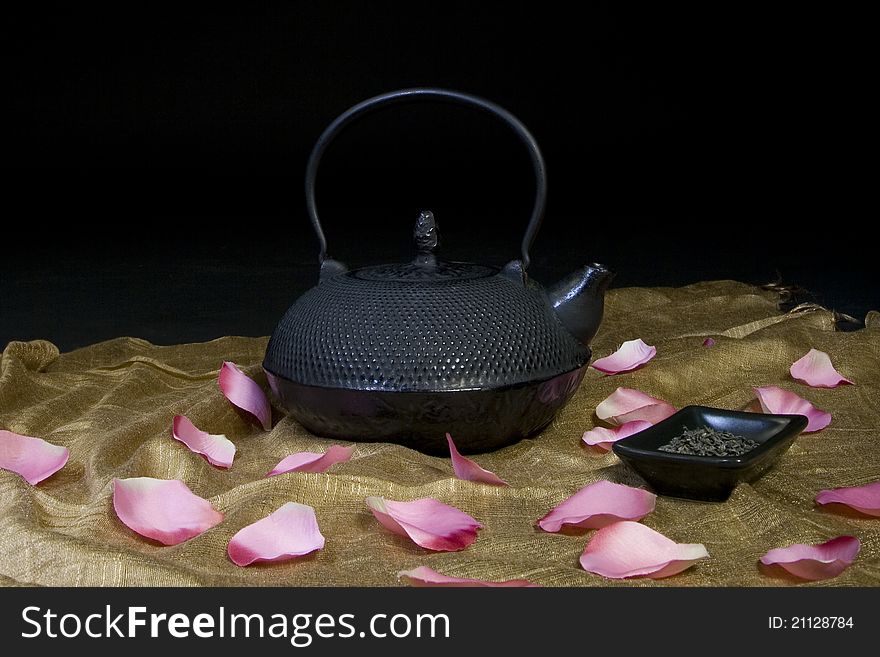 Black Chinese teapot with green tea and rose petals scattered.