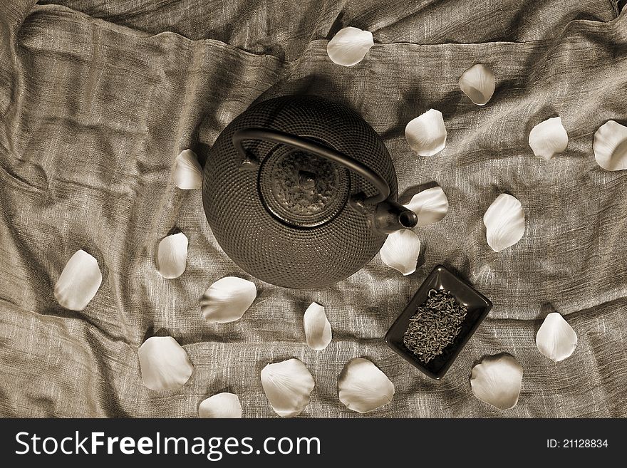 Black Chinese teapot with green tea and rose petals scattered.