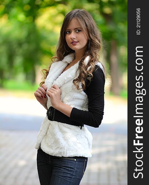 Portrait of the beautiful young girl with long hair, in the park, a holding hand with manicure on a white fur coat against green trees. Portrait of the beautiful young girl with long hair, in the park, a holding hand with manicure on a white fur coat against green trees