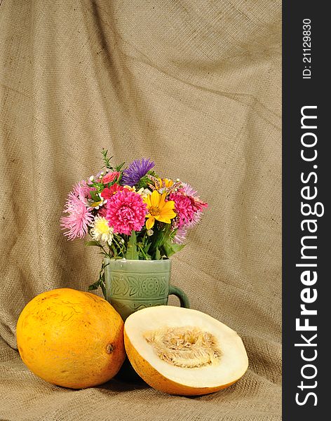 The autumn topic. In the foreground is bouquet of wild and cultivated flowers and orange melon. They are on the table covered by rough stuff. This staff creates background. The autumn topic. In the foreground is bouquet of wild and cultivated flowers and orange melon. They are on the table covered by rough stuff. This staff creates background.