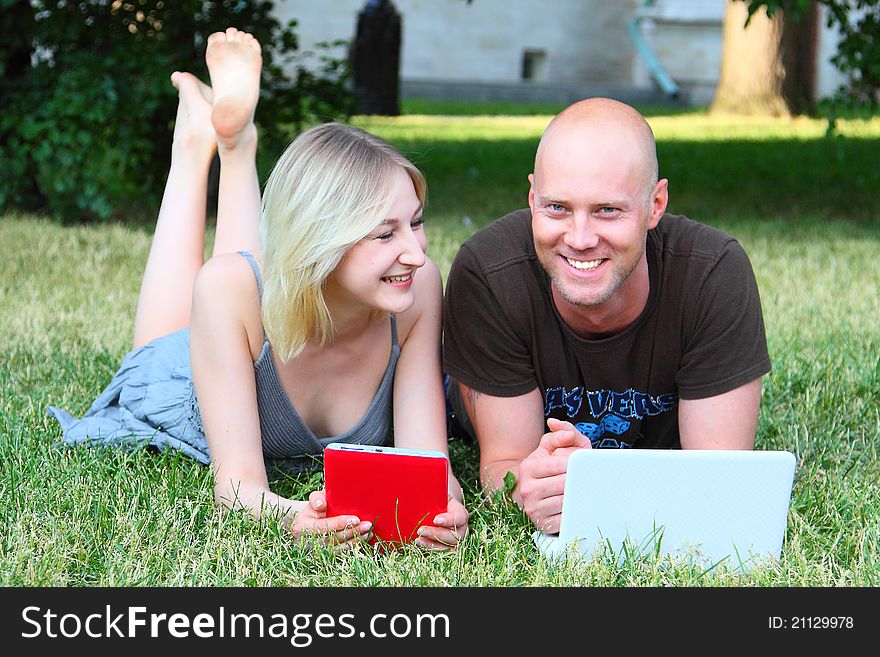 Young married couple in park with the laptop and the electronic book