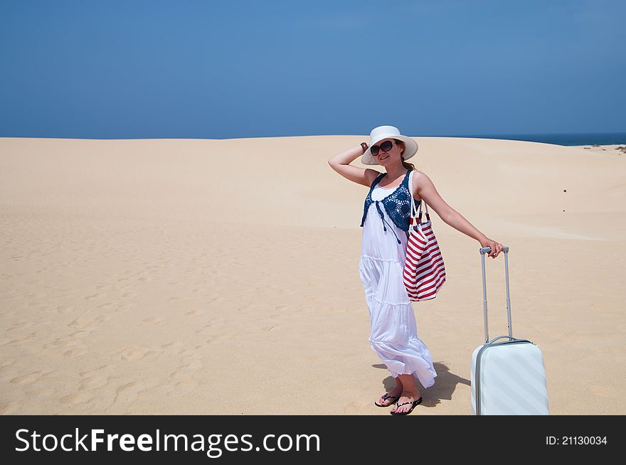 Woman holding luggage on a beach with white sand. Woman holding luggage on a beach with white sand