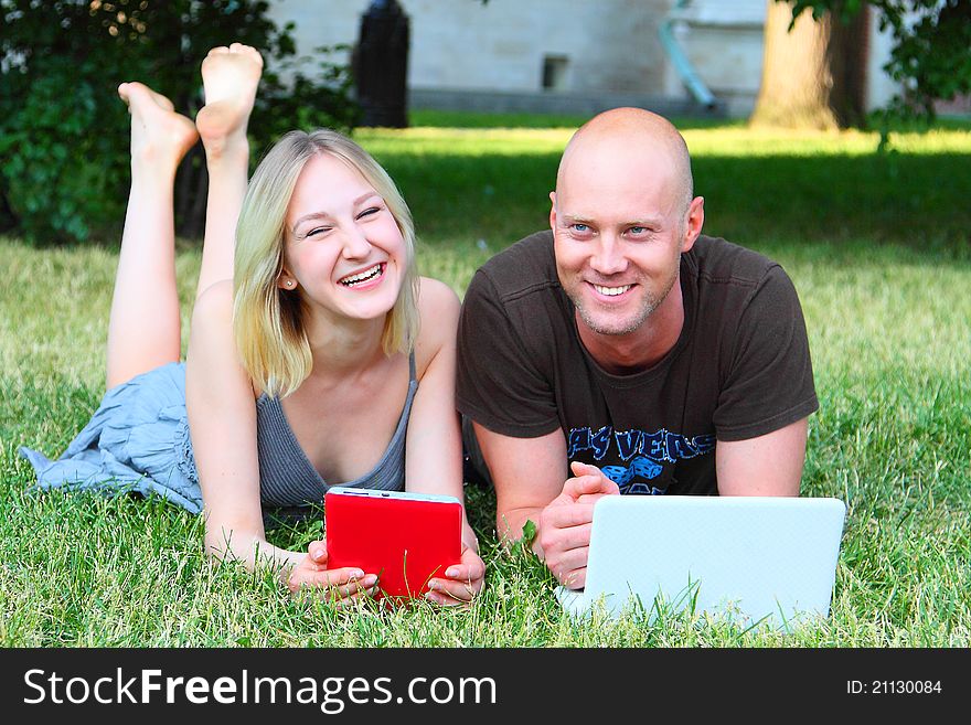 Young married couple in park with the laptop and the electronic book