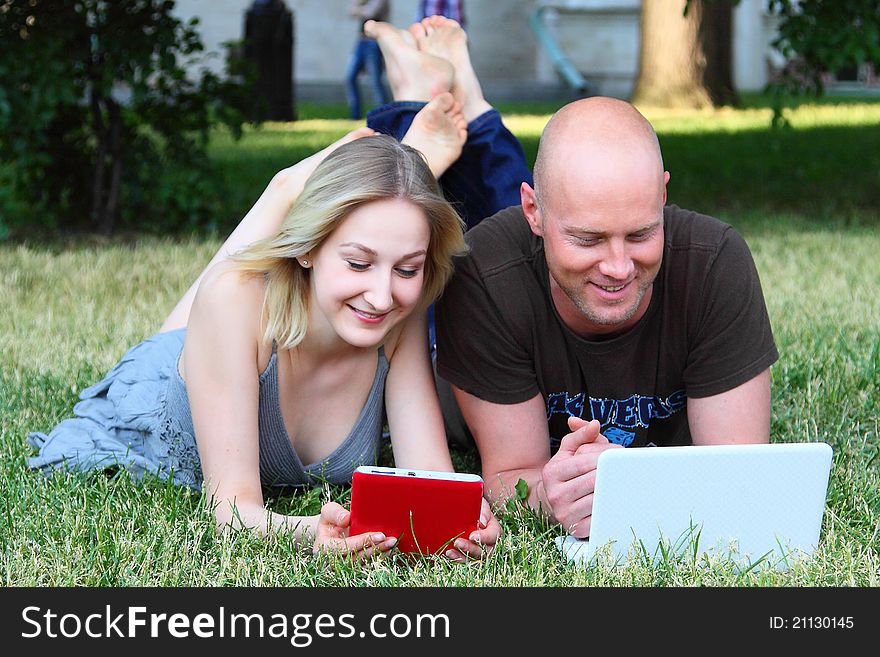 Young married couple in park with the laptop and the electronic book