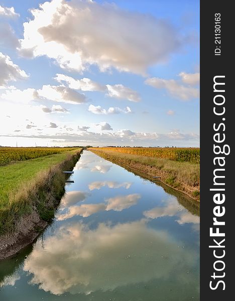 Reflections of the clouds in the water of a canal through the fields. Reflections of the clouds in the water of a canal through the fields