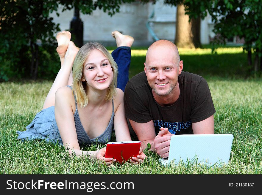 Young married couple in park with the laptop and the electronic book