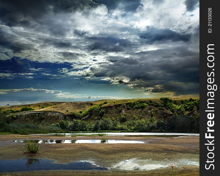 Clouds above lake and trees on coast, distant mountains are showing their tops