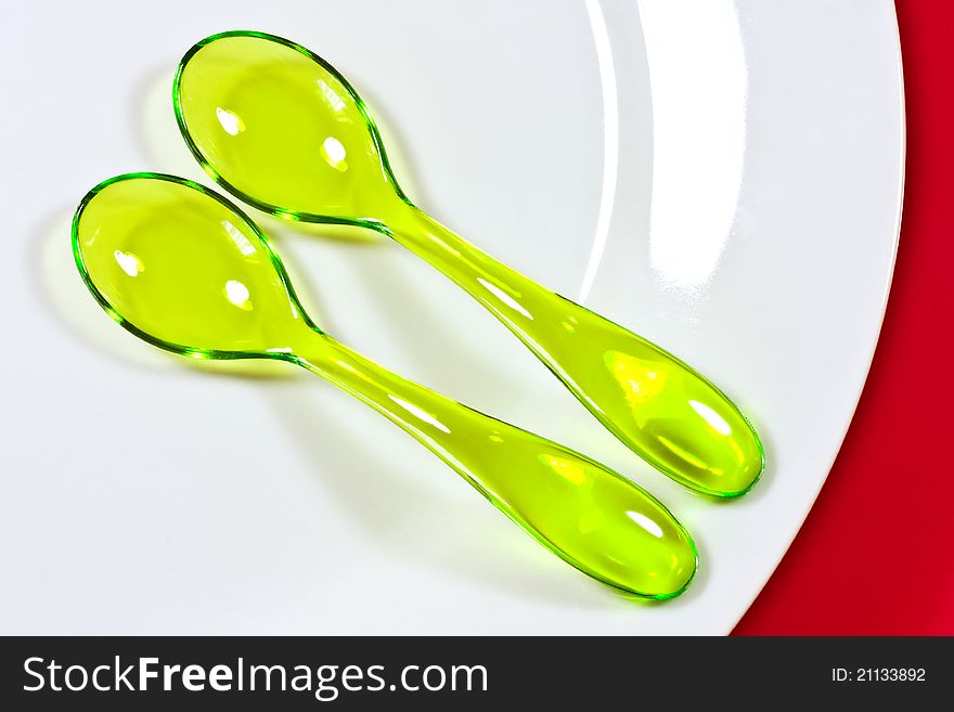 A pair of yellow plastic spoons on a white ceramic plate and red tablecloth. A pair of yellow plastic spoons on a white ceramic plate and red tablecloth.