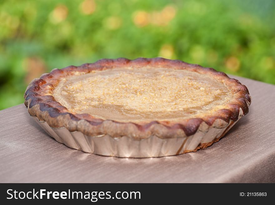 An outdoors angled closeup of a freshly baked homemade Belgian apple custard pie sitting on a tablecloth with the garden in the background. An outdoors angled closeup of a freshly baked homemade Belgian apple custard pie sitting on a tablecloth with the garden in the background.