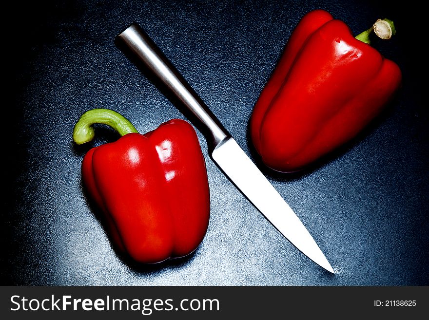 Two red peppers and a silver knife on a black background. Two red peppers and a silver knife on a black background.