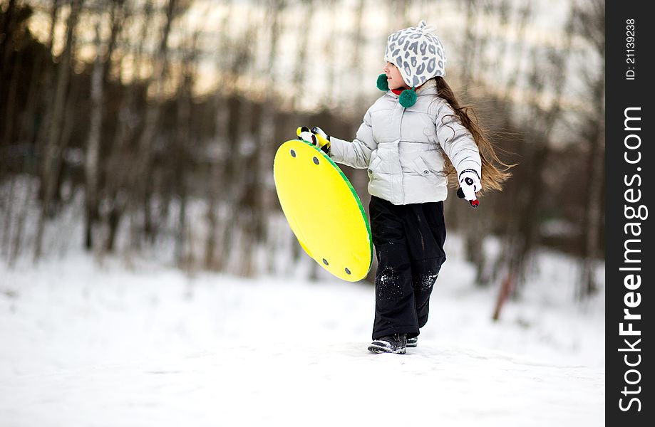 Cute little girl running in the snow with saucer