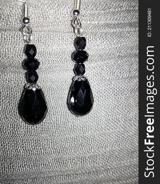 On a nice textile background texture, a photo of some beautiful black semiprecious stone with sterling silver accessories earrings, made by my mom of course. On a nice textile background texture, a photo of some beautiful black semiprecious stone with sterling silver accessories earrings, made by my mom of course