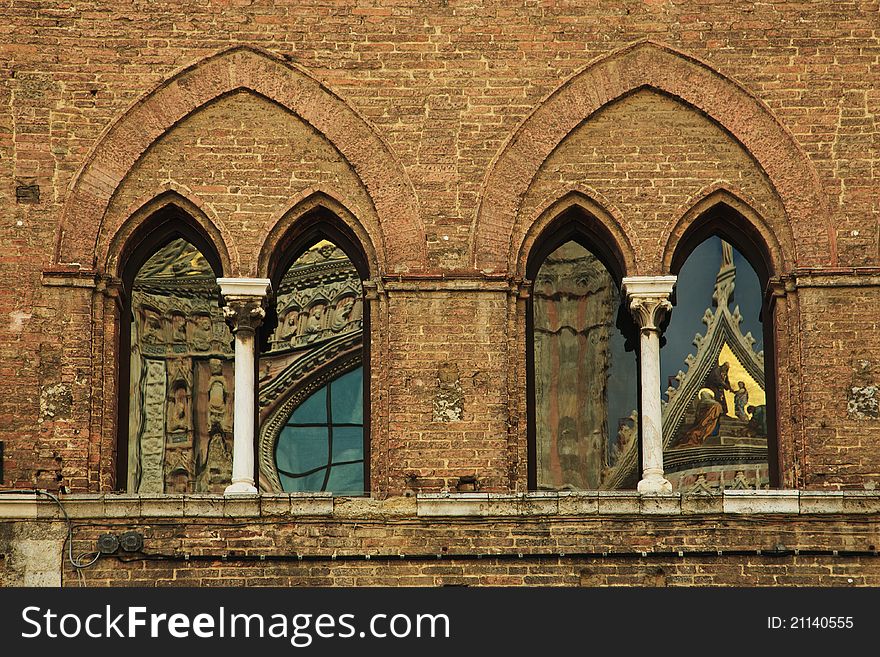 The large windows in a building across from the main cathedral in Siena, Italy, with interesting reflections of the cathedral in them. The large windows in a building across from the main cathedral in Siena, Italy, with interesting reflections of the cathedral in them.