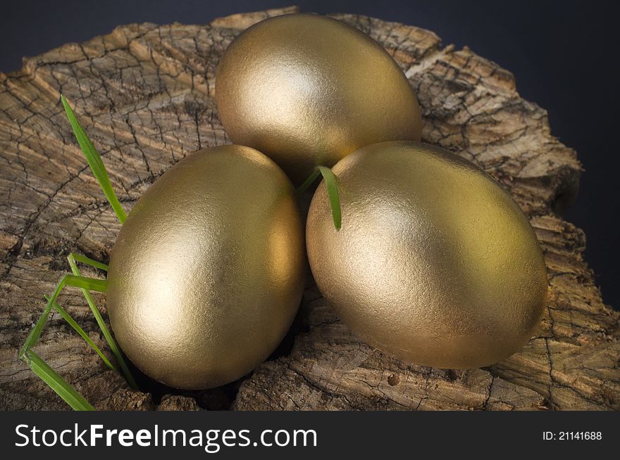 Three gold eggs on a chopping block with emerging weeds. Three gold eggs on a chopping block with emerging weeds.