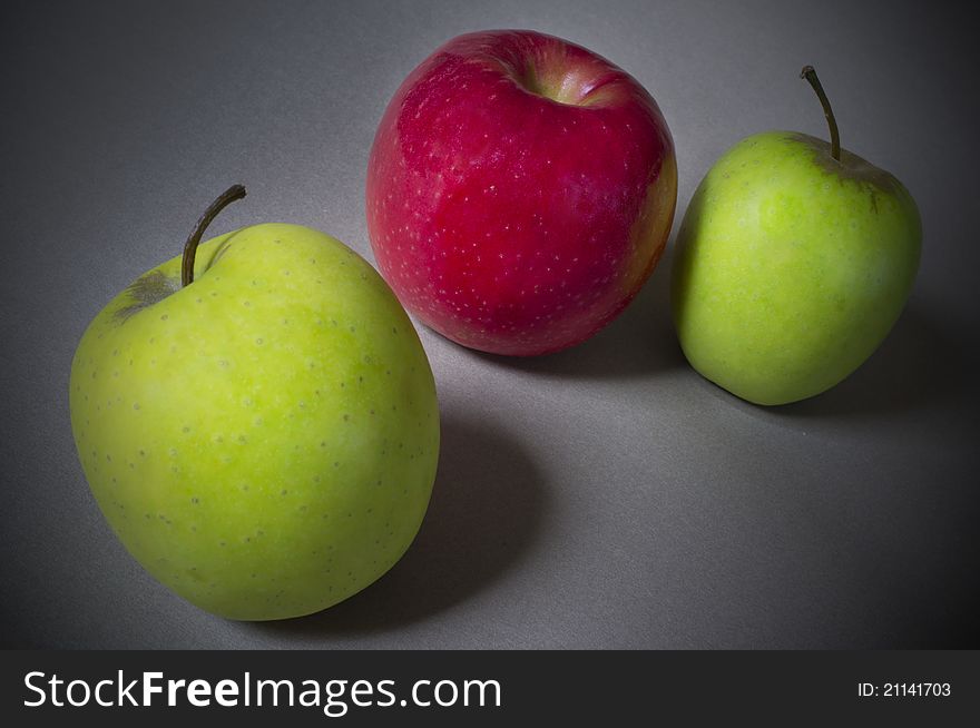 A red apple sitting between two green apples. A red apple sitting between two green apples