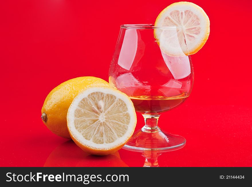 Cognac in a classic glass and lemon on a red background