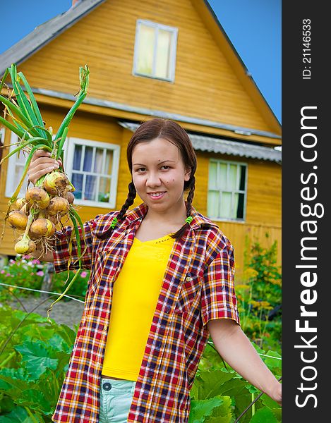 Young girl with harvested onion in field. Yellow house at the background