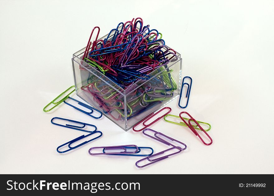 Brightly colored paperclips spilling out of a square, clear acrylic holder. Brightly colored paperclips spilling out of a square, clear acrylic holder.