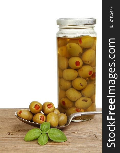 Olives in a spoon with a jar of olives and basil herb on an old wooden board. Olives in a spoon with a jar of olives and basil herb on an old wooden board