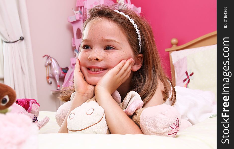 A happy young girl lies on a bed in a bright pink room.