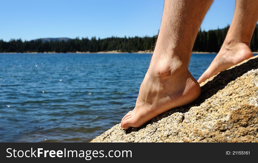 Mans Feet on big yellow rock near blue deep lake on sunny day. Mans Feet on big yellow rock near blue deep lake on sunny day