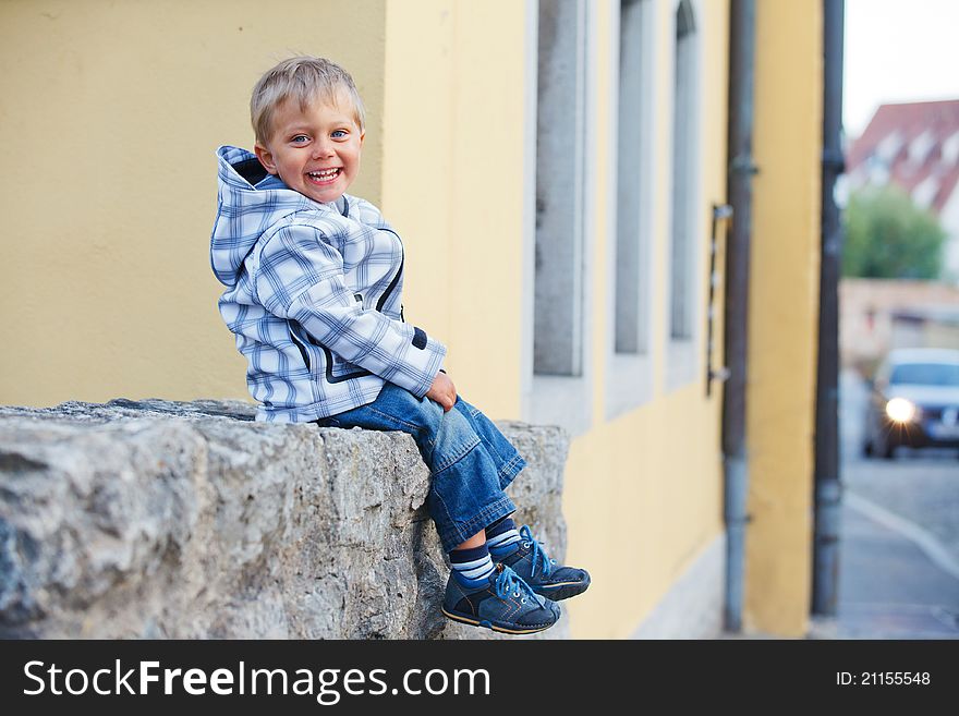 Cute little boy sits near the old house on a city street. Germany