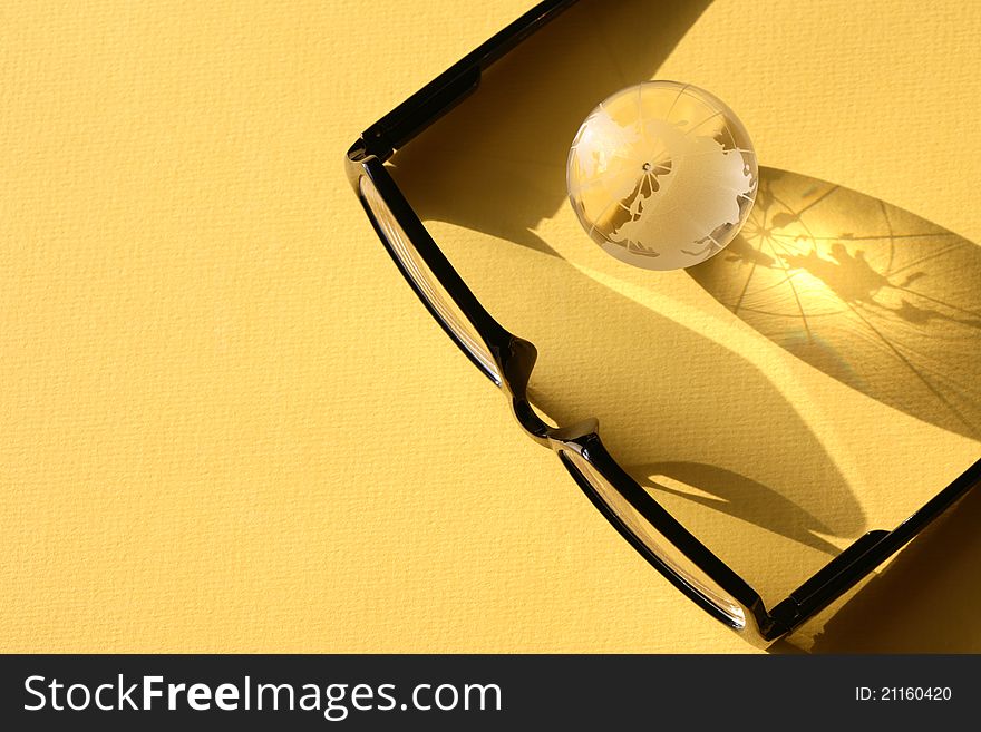 Business concept. Glass globe near modern black spectacles on yellow surface. Business concept. Glass globe near modern black spectacles on yellow surface