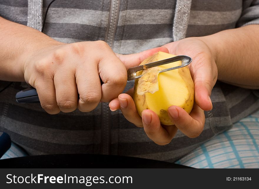 A close up of a persons hands peeling potatoes with a potato peeler.