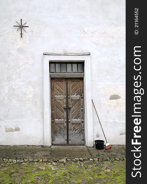 Street. An entrance in monastery. Cross and sun, metal sign. A broom and a bucket for garbage