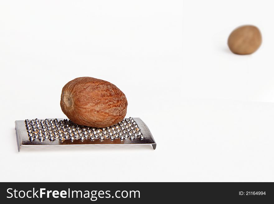 One nutmeg on a grater, with other in the upper right corner, isolated on white background. One nutmeg on a grater, with other in the upper right corner, isolated on white background.