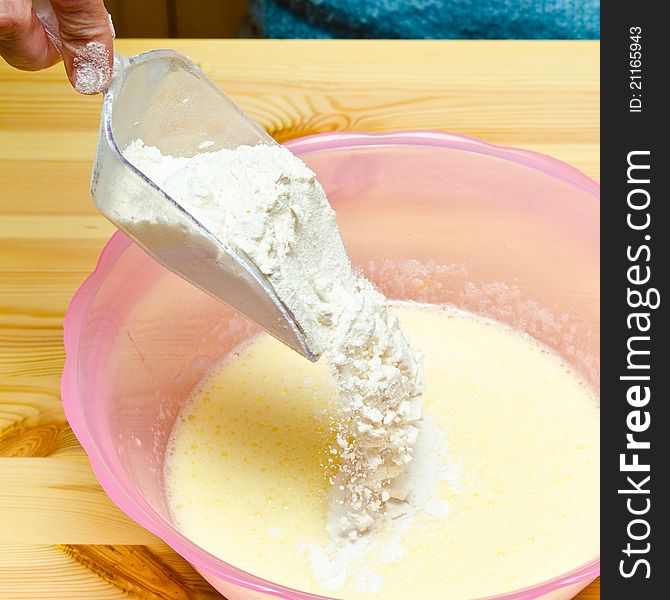 Making cookies. Pouring flour into a pink bowl on wooden table.